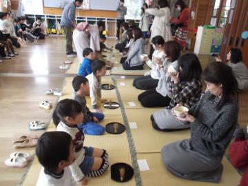 畳の上で、子どもたちが親と向かい合って座り、抹茶のおもてなしをしている写真