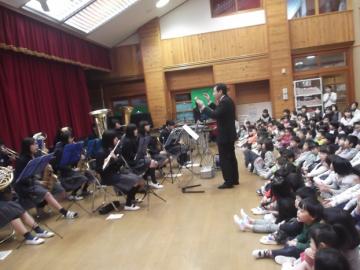 子供たちが、吹奏楽部の生徒の前に座って、演奏を聴いている写真