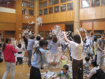 保護者と子どもたちが新聞紙を破って上に投げたり、遊んでいる様子の写真