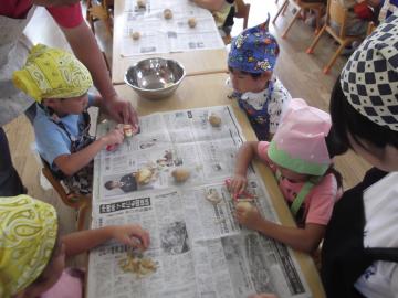 子どもが新聞紙の上でピーラーを使って野菜の皮むきをしている写真