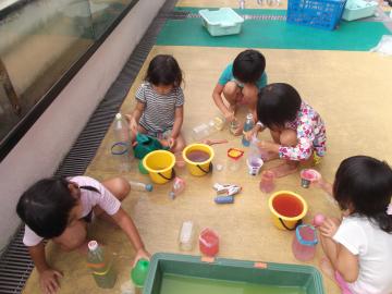 年中児が水に色を入れて実験する水遊びの様子の写真