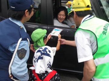 年中児が女性警察官と一緒にドライバーに手拭いを渡している様子の写真
