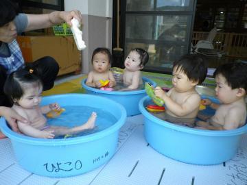 大きなたらいの中で温水に入って遊ぶ0歳児らの写真