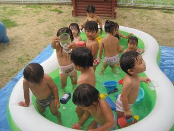 ビニールプールで水遊びを楽しむ1歳児らの写真