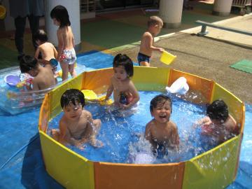 ビニールプールで水遊びを楽しむ2歳児らの写真