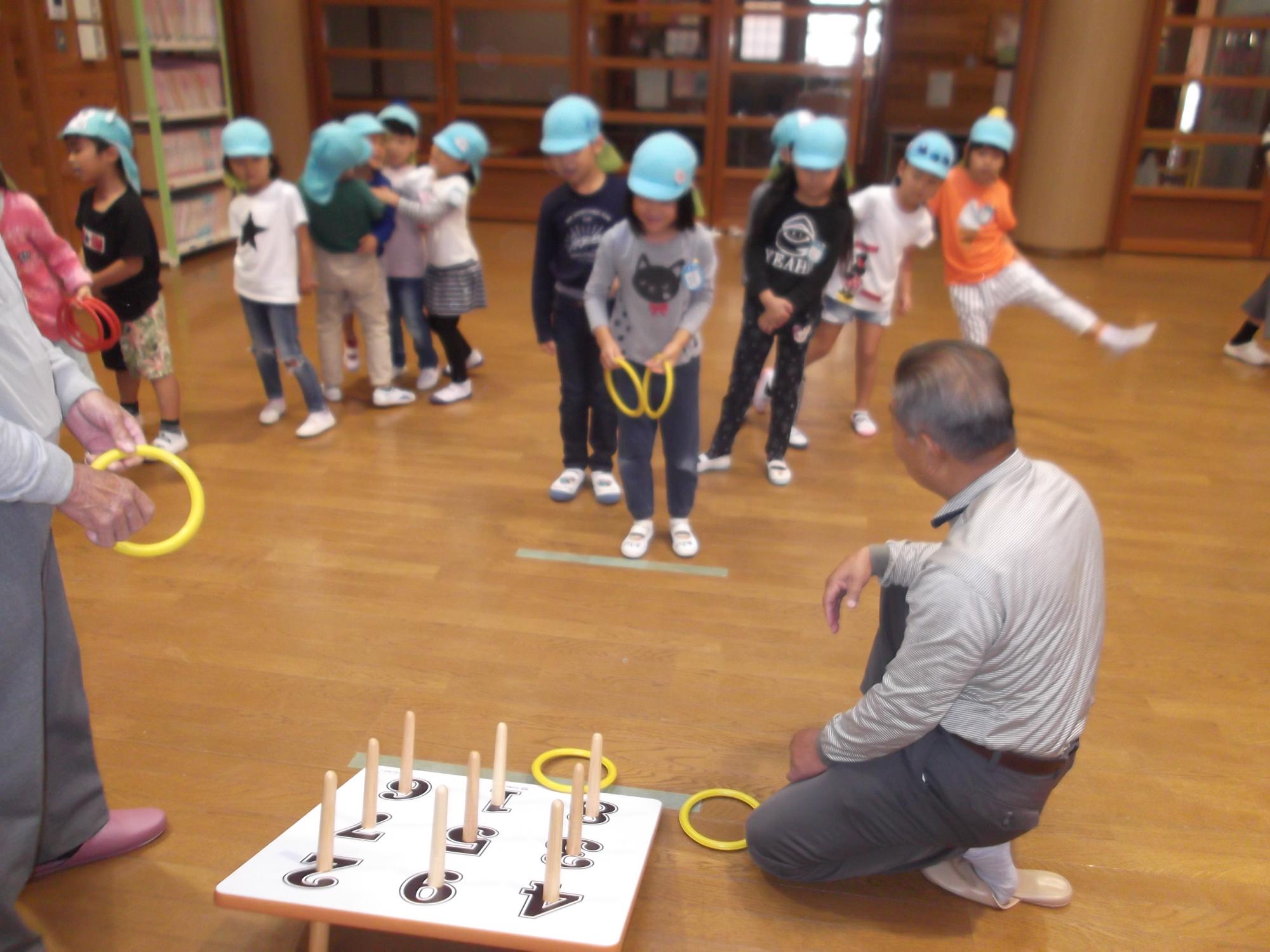 老人クラブの方たちが見守る中輪投げで遊んでいる子どもたちの写真