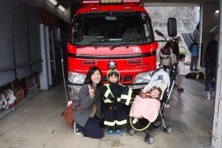 消防士の衣装を着た子供と母親とベビーカーに乗った赤ちゃんが消防車の前で撮影した記念写真
