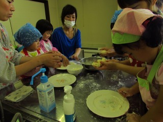 三角巾を付けた子供たちが粉を振った作業台の上で小麦粉をこねている写真
