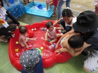 赤いプールに入っている3人の赤ちゃんが水浴びしている写真