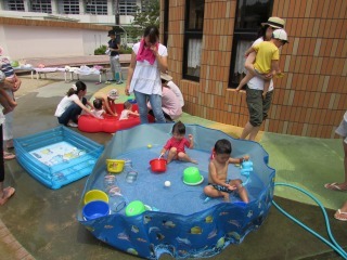 バケツなどのおもちゃが入っている青色の大きいプールで、3歳の男の子と女の子が遊んでいる写真