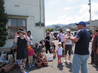 説明をしている府山城北農業改良普及センターの職員と種のまき方を教えてもらっている参加者親子の写真
