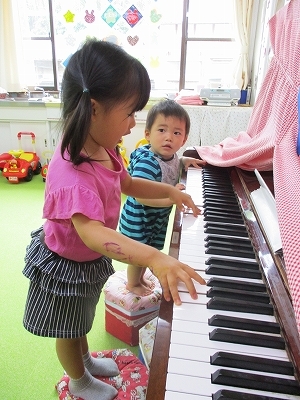 ピアノの弾き語りをする女の子と、それを見る男の子の写真