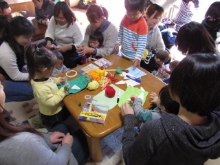 参加者親子が机の周りに集まって、画用紙やマジック、のりを使って製作を楽しんでいる写真