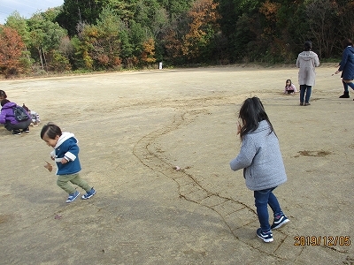 子どもたちが砂に描いた線路で電車ごっこで遊んでいる写真