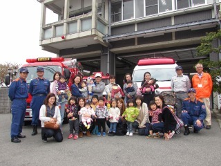 消防署の前に停車している救急車と消防車の前で参加親子たちが記念撮影している写真