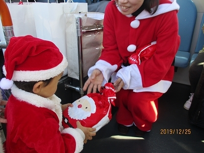 サンタの格好をした子どもがバスの中でクリスマスプレゼントをもらっている写真