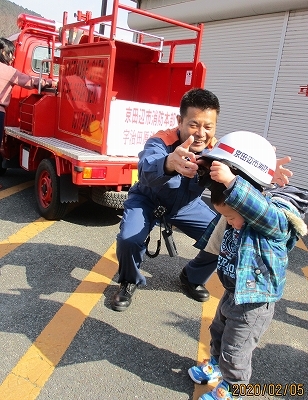 消防士の方にヘルメットを被せてもらう男の子の写真