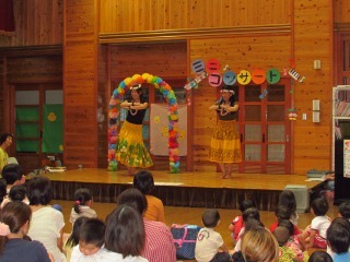 舞台の上で頭に花飾りを付けた女性二人がフラダンスを踊っている写真