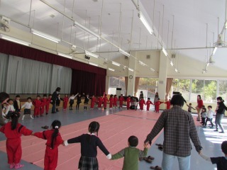 支援センターの親子とうぐいす幼稚園の園児が一緒に手をつないで大きな一つの円を作ってわらべうたをしている写真
