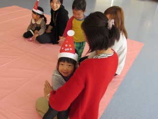 サンタクロースの帽子を作ってかぶっている女の子が笑顔でママの膝に座っている写真