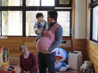 妊娠シミュレーターを着用して子供を抱いている男性の写真