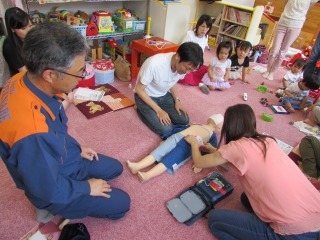 男性と女性が幼児用人形でAEDの使い方を習っている写真
