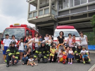 消防車と救急車の前に親子連れや消防士が集まっている集合写真
